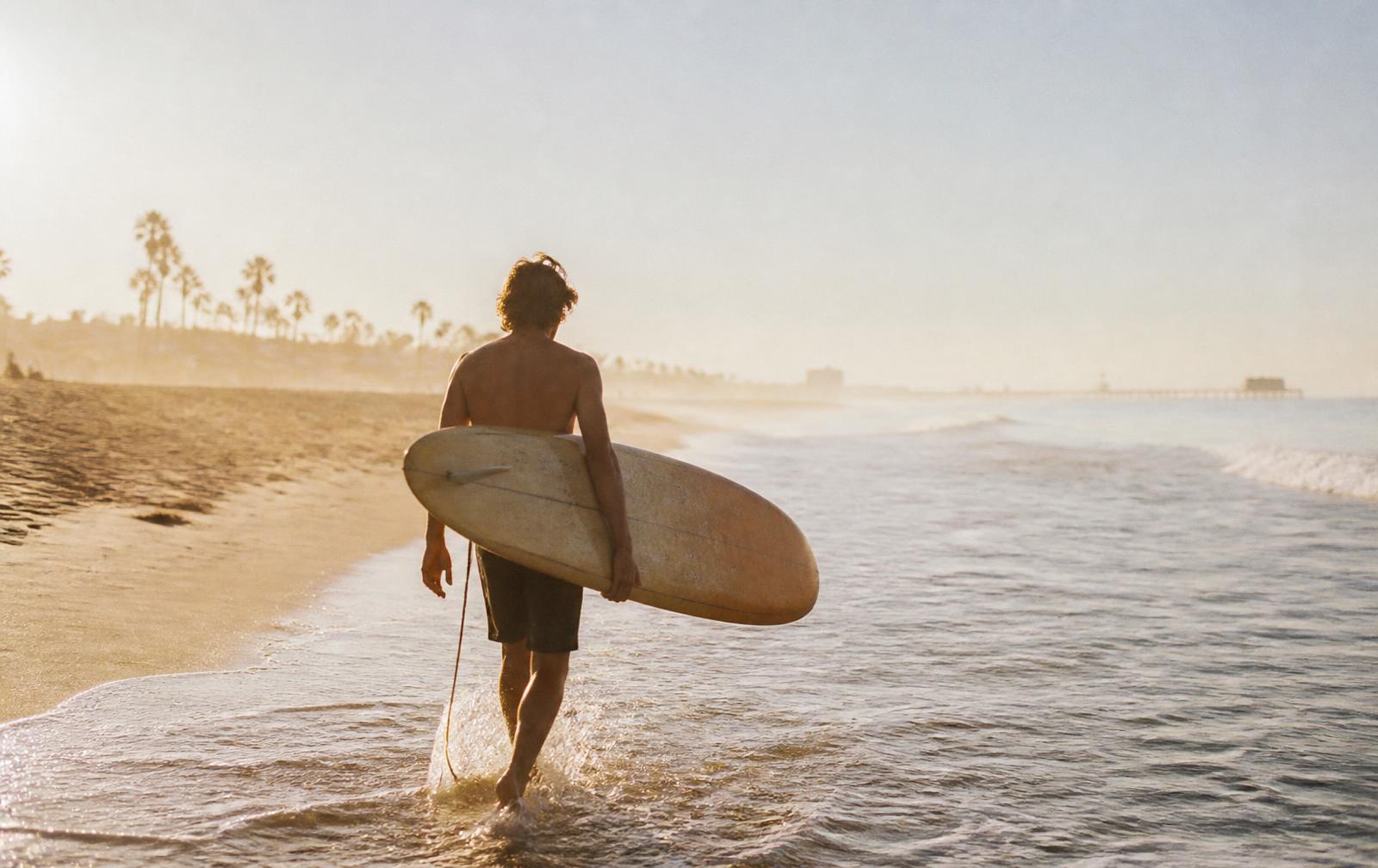 A surfer walking into the shorebreak at golden hour, Venice, California